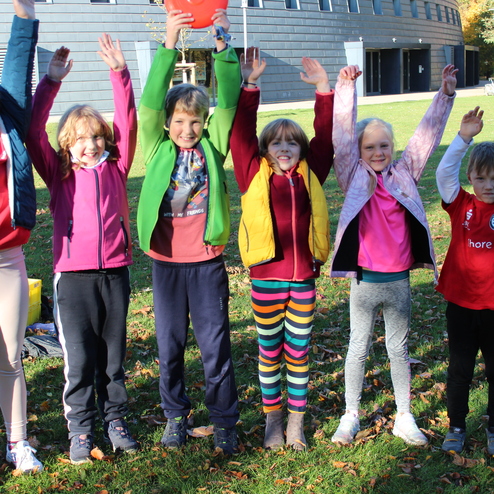 Hier siehst du Kinder, die in einer Reihe stehen und die Arme hochstrecken.