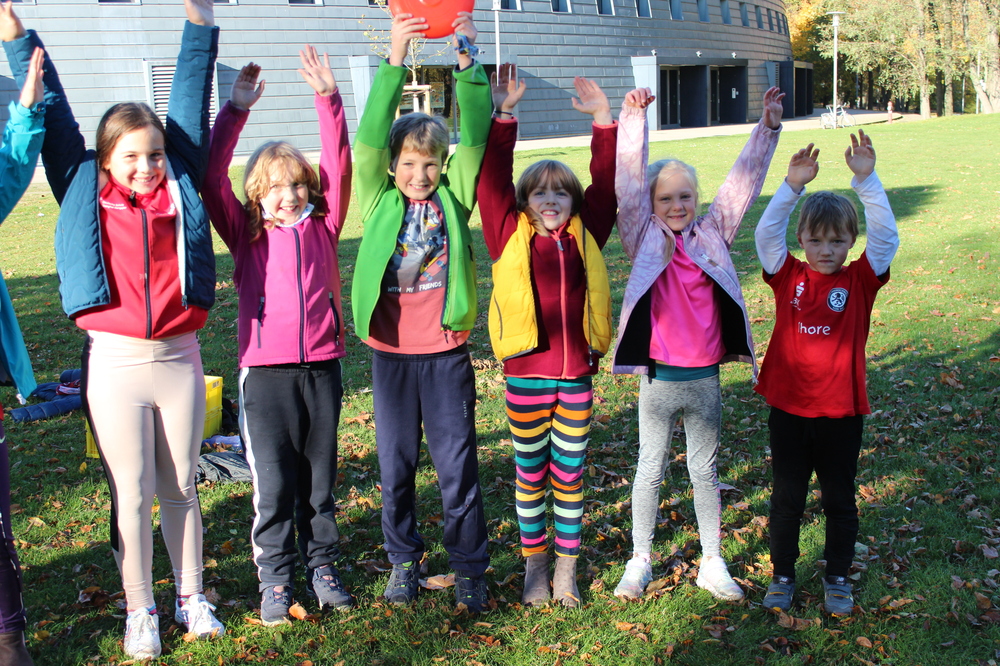 Hier siehst du Kinder, die in einer Reihe stehen und die Arme hochstrecken.