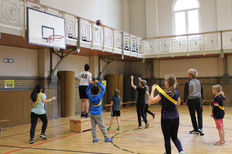 Hier siehst du Kinder in einer Turnhalle. Sie sind am Basketball spielen.