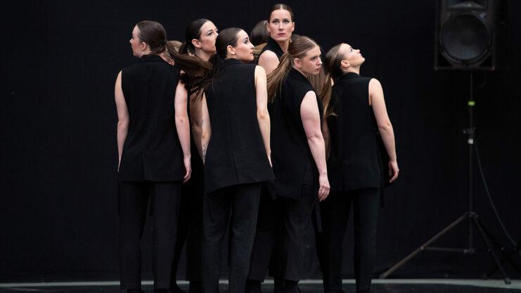 Hier siehst du unsere Turniertanzgruppe "Leonas". Sie haben schwarze Turnieroutfits an, stehen in der Gruppe und schauen über ihre Schulter.