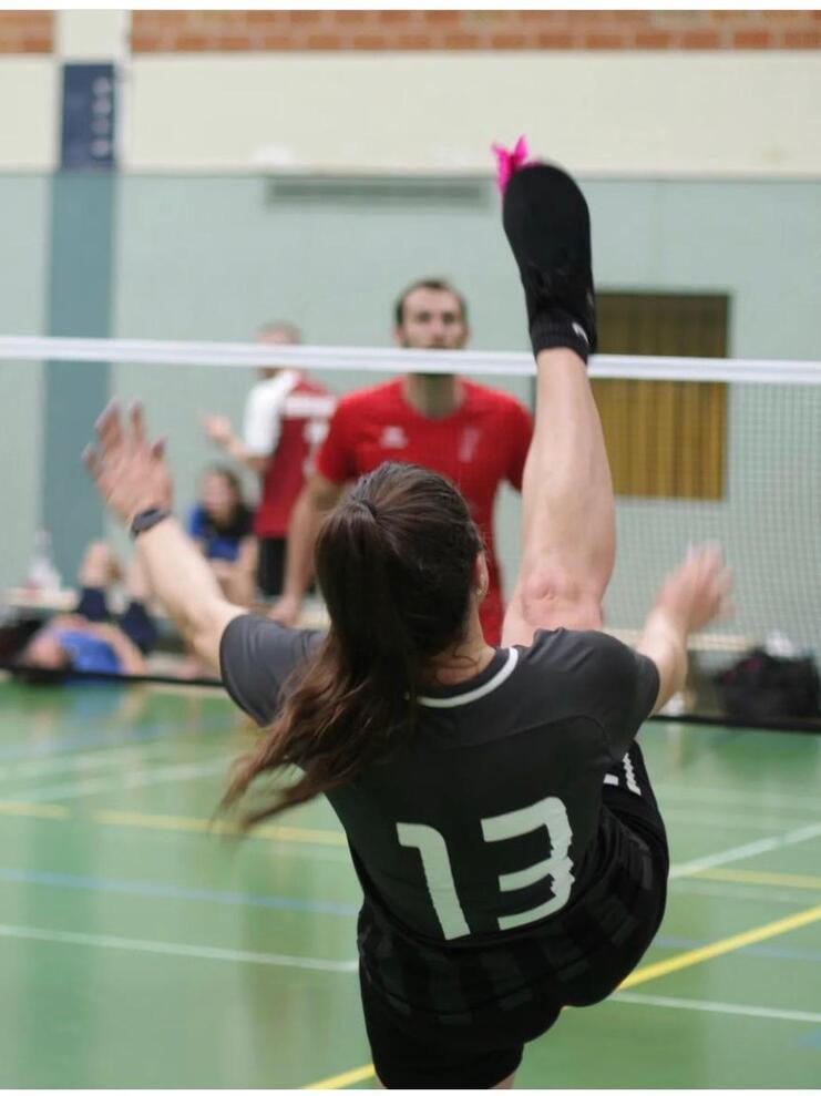 Hier siehst du eine Frau, die einen Federfussball über ein Netz schießt.