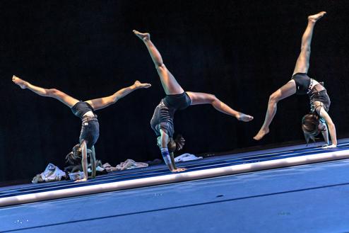 Hier siehst du drei Turnerinnen die ein Rad schlagen.
