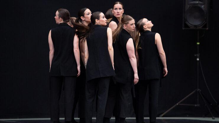 Hier siehst du unsere Turniertanzgruppe "Leonas". Sie haben schwarze Turnieroutfits an, stehen in der Gruppe und schauen &uuml;ber ihre Schulter.