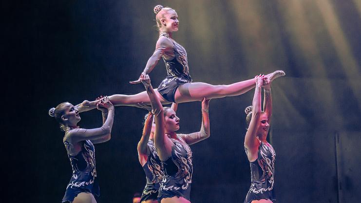 Hier sind vier Frauen, die eine weitere im Spagat über ihren Kopf tragen.