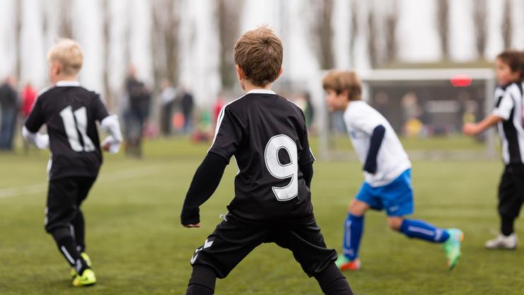 Kinder spielen Fußball auf einem Sportplatz; ein Spieler trägt ein schwarzes Trikot mit der Nummer 9.