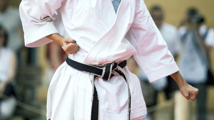 Nahaufnahme eines Karateka in Weiß mit schwarzem Gürtel, der eine Faustballenposition einnimmt.