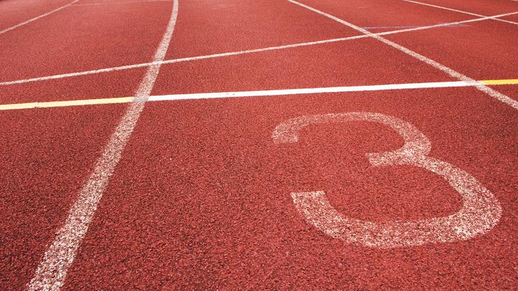 Nahaufnahme eines roten Laufbahnabschnitts mit der Markierung der Bahn 3 und weißen Linien.