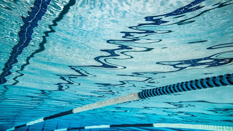 Unterwasseraufnahme eines Schwimmbeckens mit reflektierender Wasseroberfläche und Markierungen auf dem Boden.