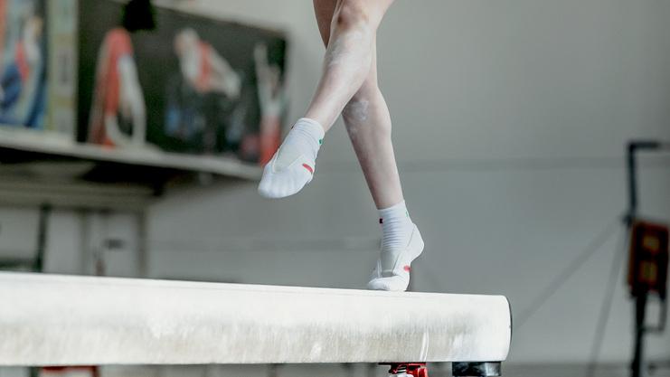 Athletisches Bein mit speziellen Turnschuhen schwebt über einem Schwebebalken in einer Trainingsumgebung.